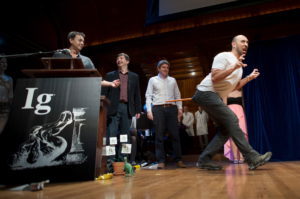 Bruno Grossi (R), walks like a dinosaur as he and his team accept the Ig Nobel Prize in Biology for observing that when you attach a weighted stick to the rear end of a chicken, it then walks in a manner similar to that in which dinosaurs are thought to have walked, at the 25th First Annual Ig Nobel Prizes awards ceremony at Harvard University in Cambridge, Massachusetts September 17, 2015. The annual prizes, meant to entertain and encourage global research and innovation, are awarded by the Annals of Improbable Research as a whimsical counterpoint to the Nobel Prizes. REUTERS/Gretchen Ertl - RTS1NKR